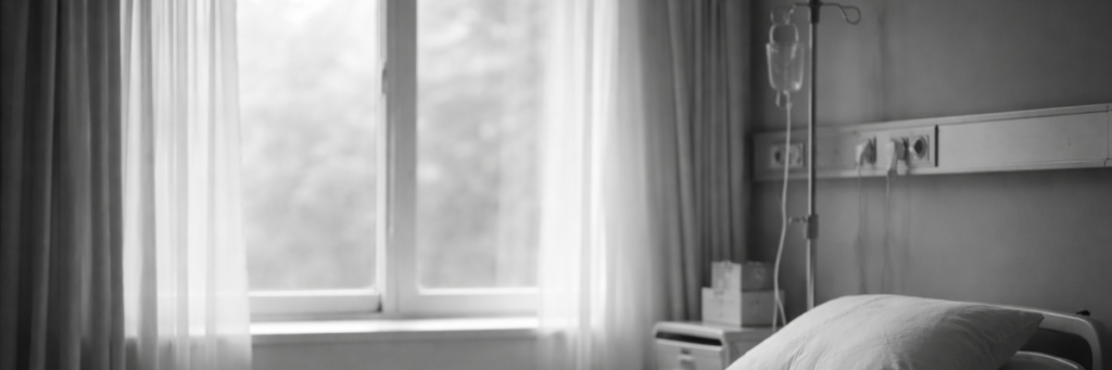病室のベッドと窓辺の光。急変が突然起きる現実を表すイメージ