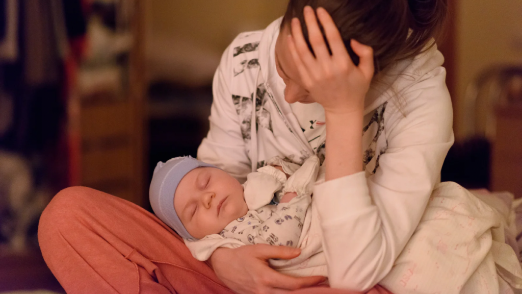 赤ちゃんを抱っこしながら頭を抱える産後ママの様子。抱っこによる姿勢崩れと腰痛のイメージ